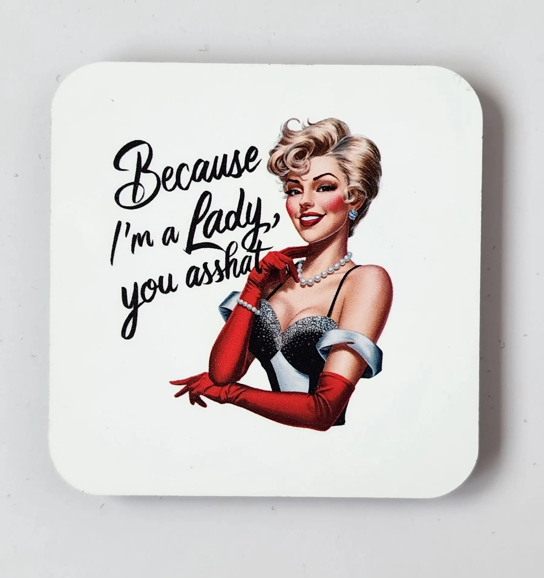 Introducing the Snarky Magnet: Because I'm a Lady You Asshat by Mirabilia Boutique. This magnet features a retro illustration of a glamorous blonde woman in a vintage strapless black and silver dress, accessorized with red gloves and a pearl necklace. With a smirk on her face, she holds a cigarette holder, and the text boldly declares, "Because I'm a lady, you asshat." A perfect statement piece for adding some sassy charm to any space.