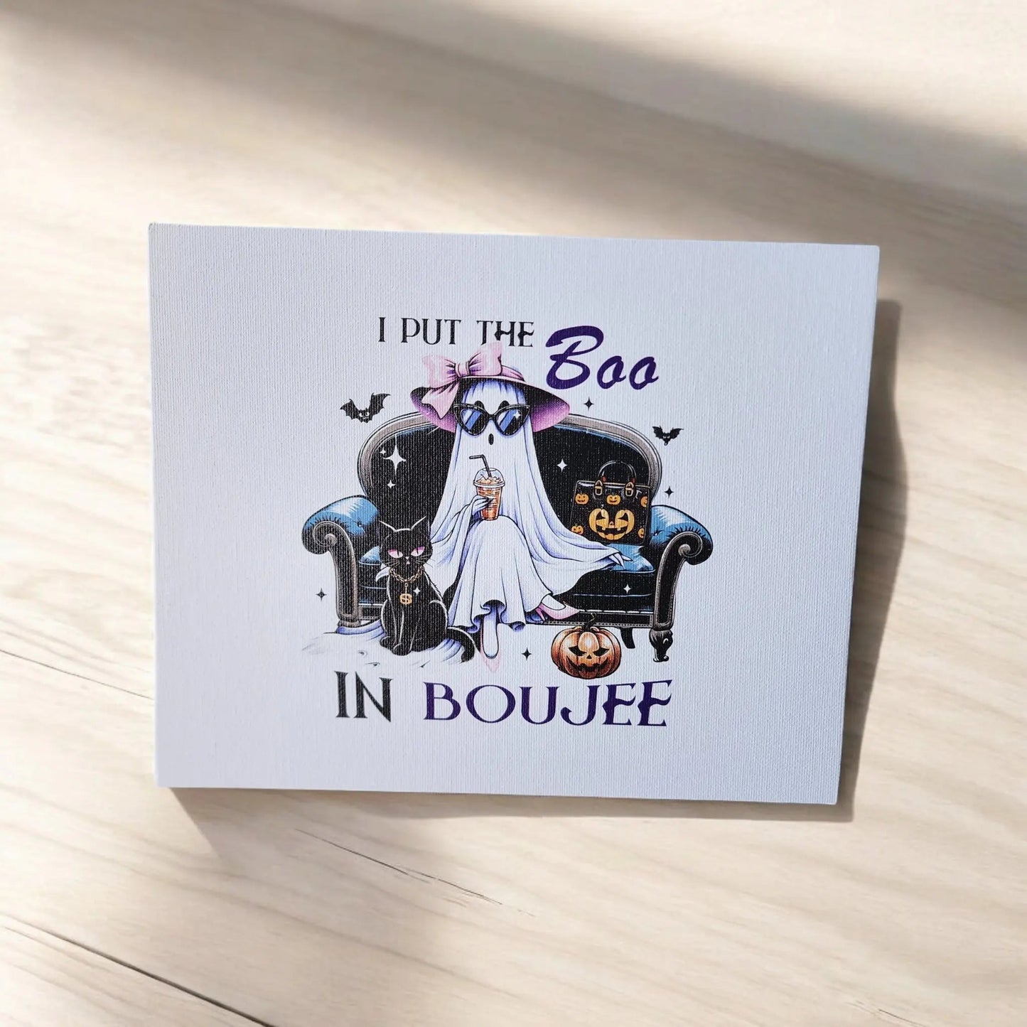 The Funny Halloween Sign: I Put the Boo in Boujee by Mirabilia Boutique is perfect for ghost enthusiasts. It features a stylish ghost wearing a hat and sunglasses, lounging on an elegant black armchair. The design includes two black cats, several pumpkins, and flying bats, with the message "I PUT THE Boo IN BOUJEE." Ideal for Halloween decor!