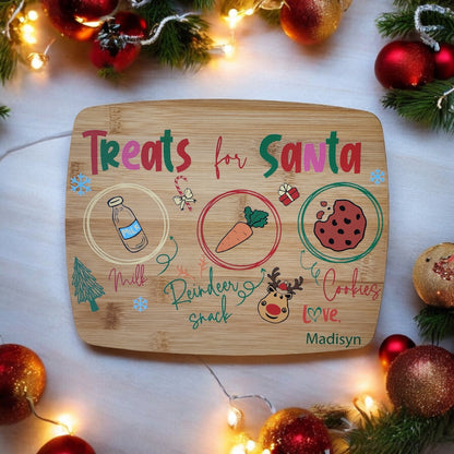 The Santa Cookie Board Personalized from Mirabilia Boutique is a charming addition to your Christmas Eve tradition, featuring sections for milk, a reindeer snack (carrot), and cookies. It is beautifully embellished with festive drawings such as snowflakes, a reindeer face, and ornaments, and bears the label "Treats for Santa," signed "love, Madisyn.