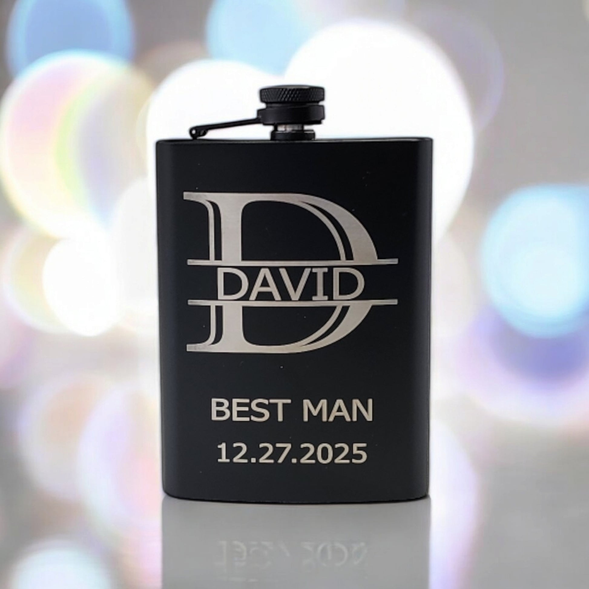 The Mirabilia Boutique's Personalized Matte Black Hip Flask, elegantly engraved with a prominent "D" and the name "David," features "Best Man" and "12.27.2025" below, creating a memorable keepsake with its subtle blurred background and gentle light effects.