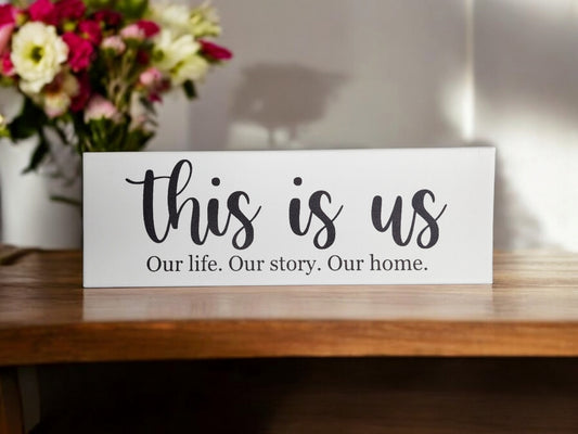 The Mirabilia Boutique "This Is Us. Our Life. Our Story. Our Home." – 4x12 Cradled Canvas-Sentimental Wall Art features elegant cursive and meaningful text, perfect for adding timeless decor to any space with its wooden charm and floral backdrop.