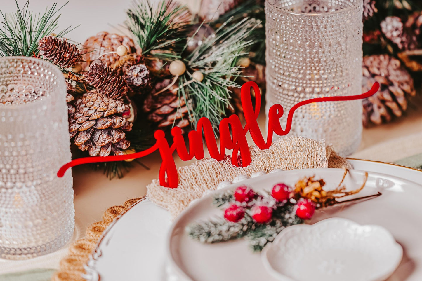 Create a holiday ambiance with Mirabilia Boutique's "Festive Christmas Plate Words for Holiday Cheer" that radiates festive decor in your tablescape. The plates, adorned with pinecones, evergreen branches, and red berries, embody the holiday spirit. Crystal glasses and a rustic centerpiece complete the display.