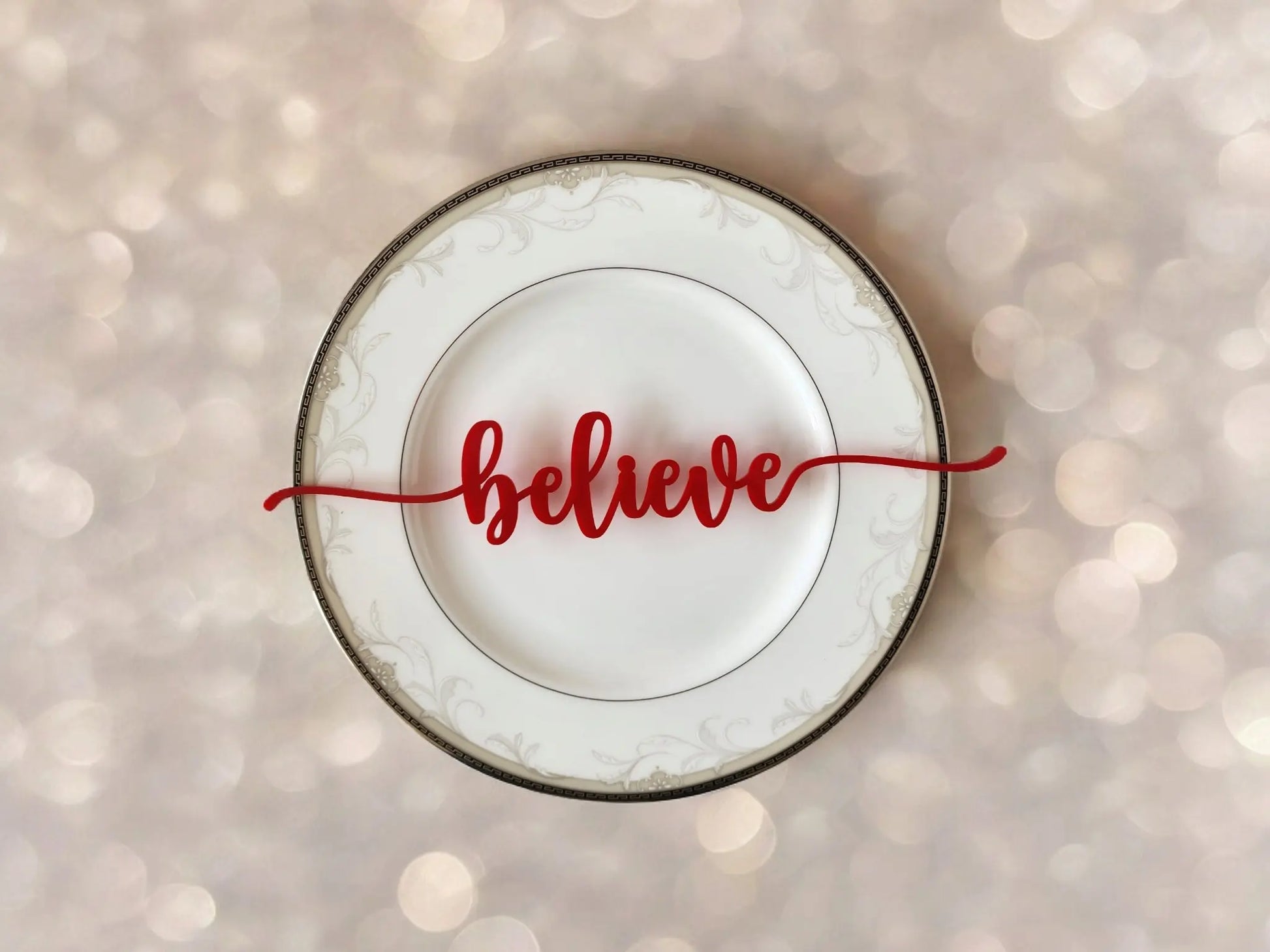 The "Festive Christmas Plate Words for Holiday Cheer" by Mirabilia Boutique features elegant patterns with the word "believe" prominently in bold, red cursive lettering. Ideal for festive decor, this plate's softly blurred background adorned with light bokeh effects creates a warm and inviting ambiance perfect for any holiday tablescape.