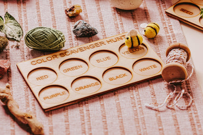 The "Exciting Color Scavenger Hunt Game for Kids' Outdoor Fun" from Mirabilia Boutique features an eco-friendly wooden board with labeled circles for colors such as red, green, and blue. This outdoor toy comes with a toy bee, rocks, yarn, and spools of string on a pink textured surface to inspire vibrant exploration.