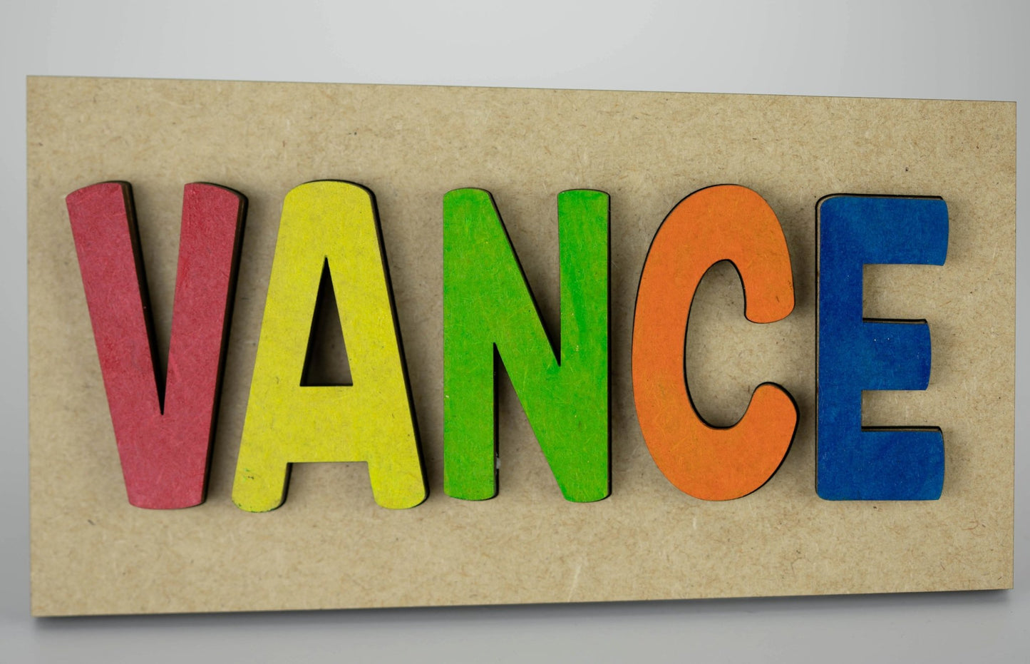 Mirabilia Boutique's Personalized Kids Name Puzzle Sign spells out "VANCE" with brightly painted wooden letters in red, yellow, green, orange, and blue to create a charming nursery decor piece. This unique educational gift is perfect against a plain background as an adorable keepsake for any baby.