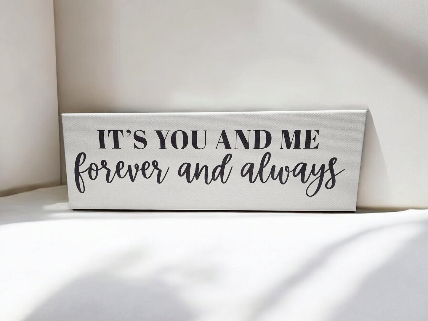 The 4x12 cradled canvas "It's You and Me Forever and Always" by Mirabilia Boutique features black typography on a white background, casting soft shadows to enhance this romantic wall art piece.