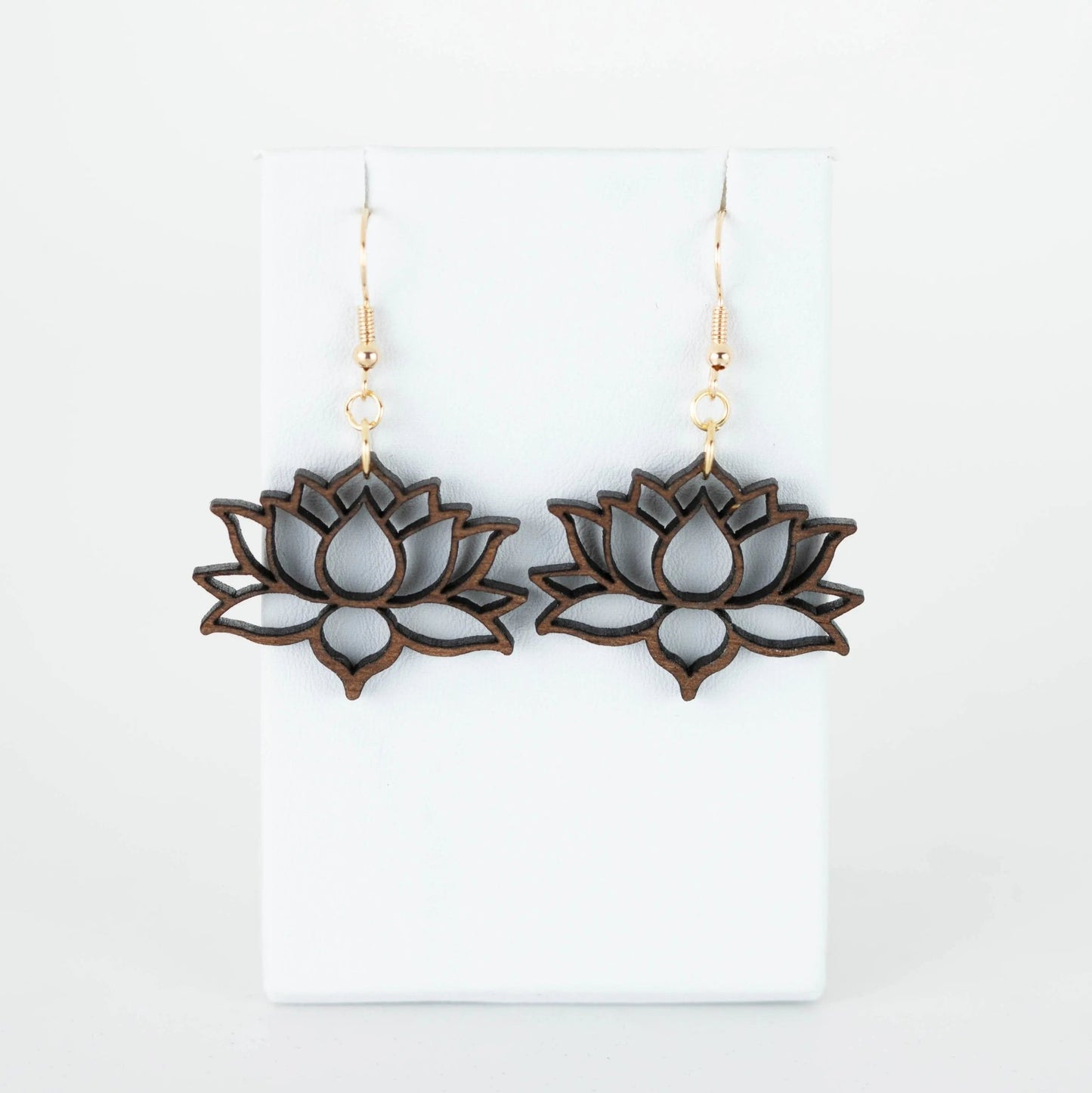 These hypoallergenic Lotus Flower Drop Earrings from Mirabilia Boutique showcase a lotus blossom design with detailed cutouts, gracefully suspended on gold hooks against a simple white backdrop.