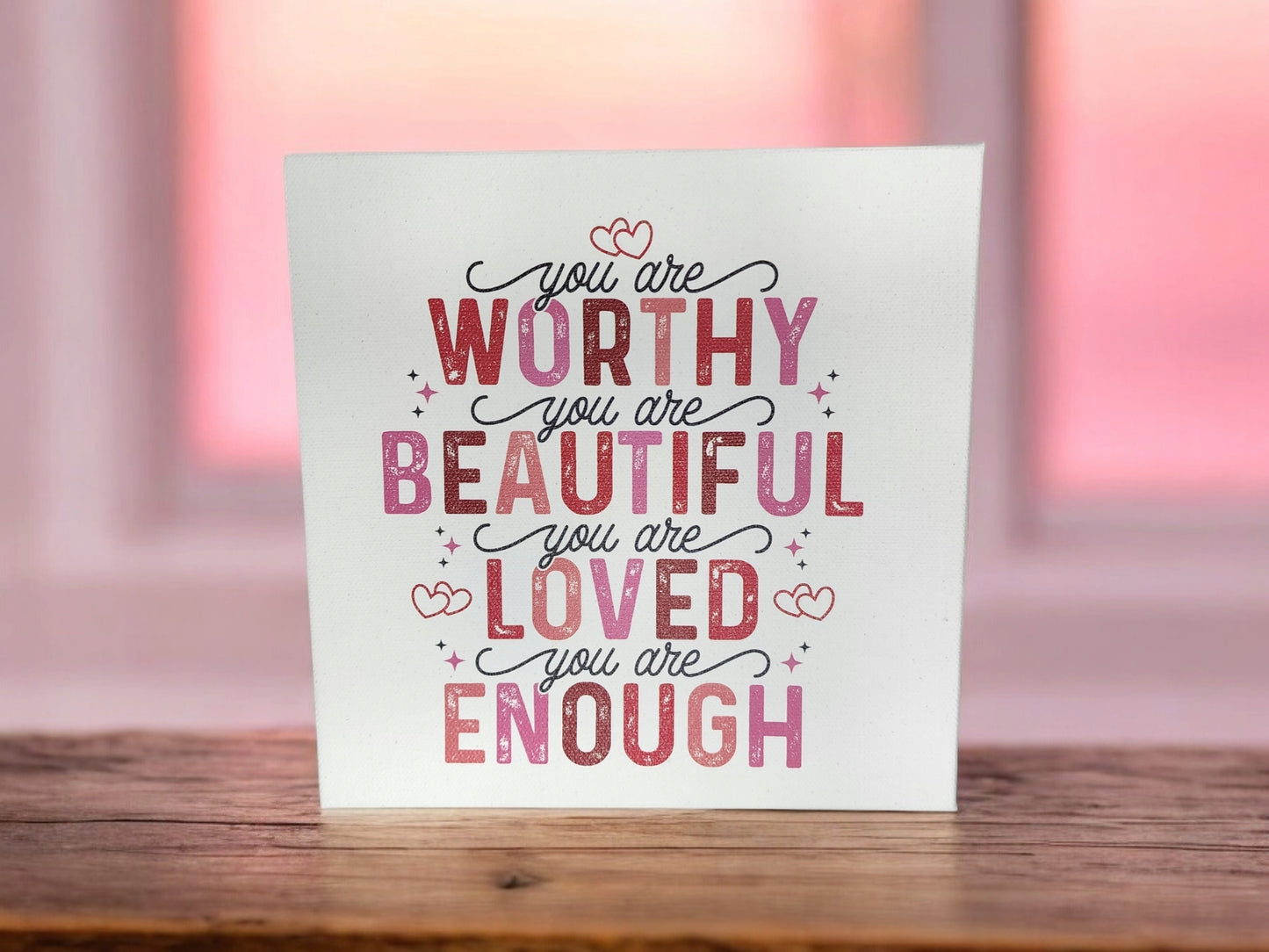 The "You Are Worthy, Beautiful, Loved, Enough" 8x8 Cradled Canvas Sign by Mirabilia Boutique features empowering affirmations in pink and red lettering with heart accents on blurred pink and orange hues, perfect for adding warmth to any home decor.