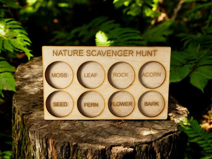 The "Nature Scavenger Hunt for Kids: Fun Outdoor Adventure Game" by Mirabilia Boutique is an eco-friendly wooden board featuring eight labeled circles, including "Moss," "Leaf," "Rock," "Acorn," "Seed," "Fern," "Flower," and "Bark." This charming outdoor toy can be found nestled on a tree stump, surrounded by vibrant green foliage.