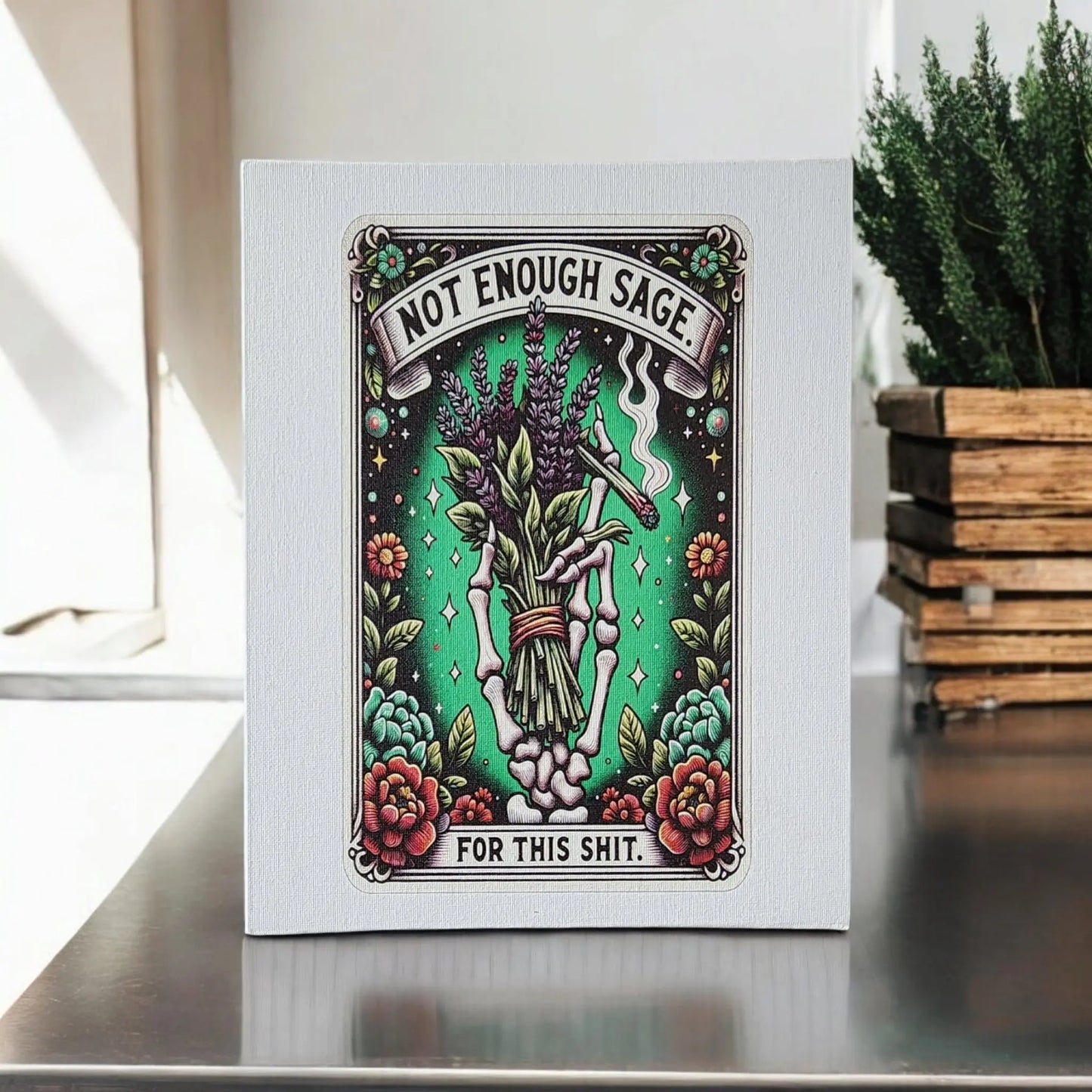 The Mirabilia Boutique Humorous Sage Quote Wall Art Print features a skeleton hand clutching sage and lavender, surrounded by colorful flowers. The playful phrase, "Not Enough Sage for This Shit," adds a cheeky touch, making it an ideal humorous gift. Perfectly suited for display on a tabletop next to stacked wooden boxes.