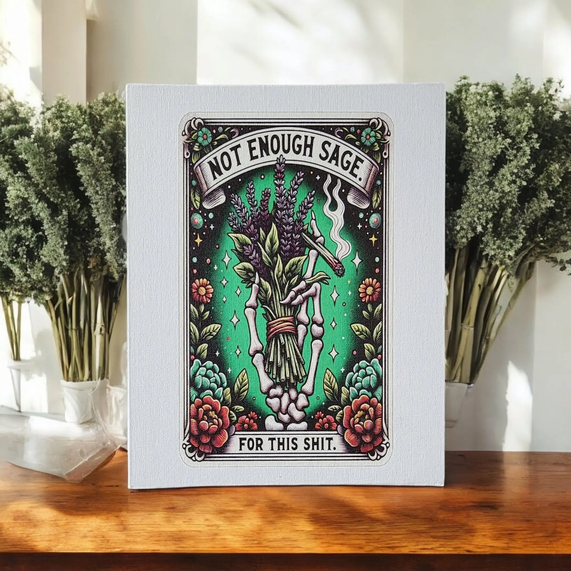 Presenting the Humorous Sage Quote Wall Art Print for Home or Office Decor by Mirabilia Boutique. This delightful piece features a vintage skeleton hand clutching sage, encircled by flowers. The playful inscription, "Not Enough Sage for This Shit," adds a touch of wit and charm to any space. Displayed perfectly on a wooden surface with plants in the background, this artwork is ideal for those who appreciate humor and style.