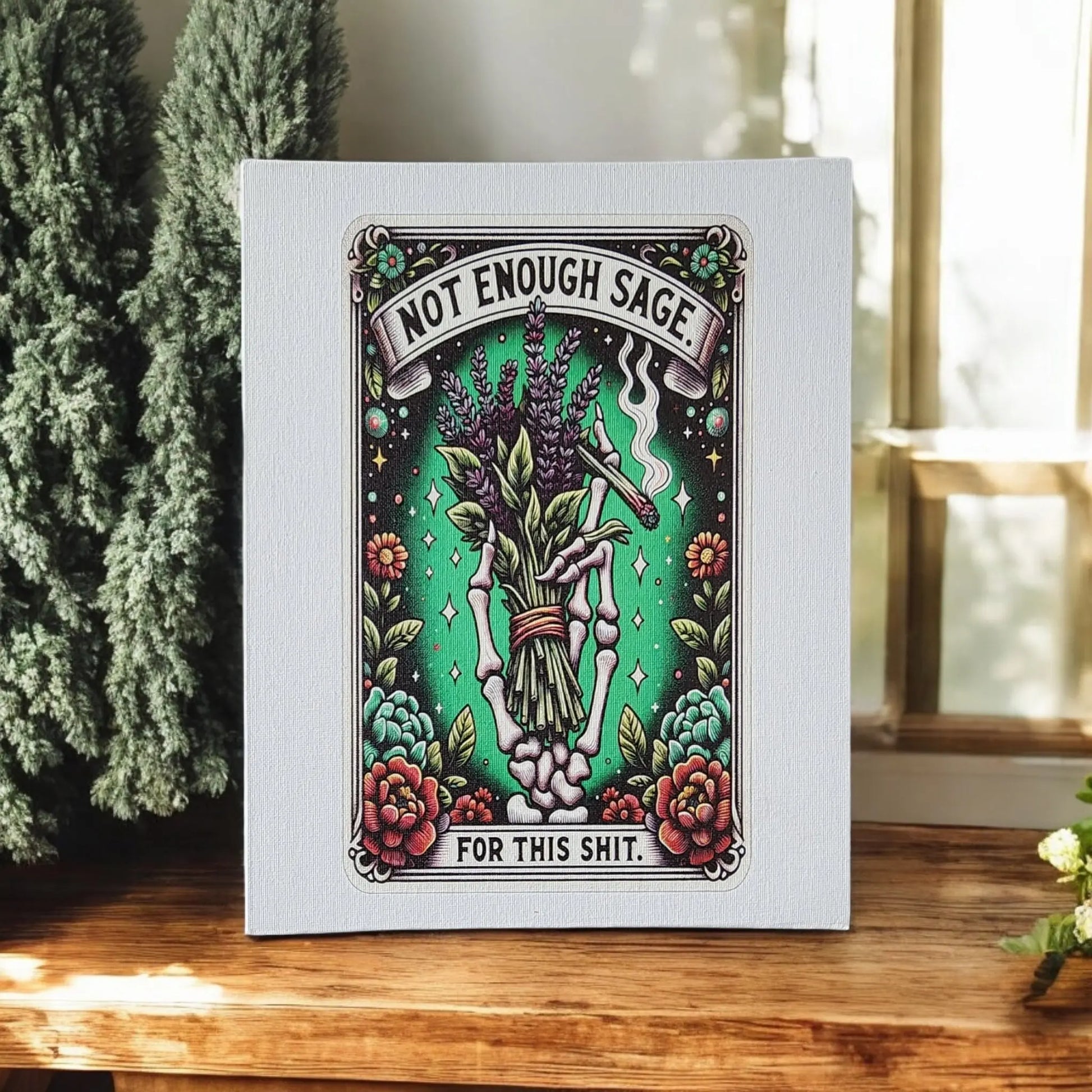 The "Humorous Sage Quote Wall Art Print for Home or Office Decor" by Mirabilia Boutique features a skeletal hand holding sage, accompanied by flowers and herbs. Displayed on a green background with the playful message "Not Enough Sage for this Shit," this decorative piece is an ideal humorous gift, perfect for showcasing on a wooden surface near a window.