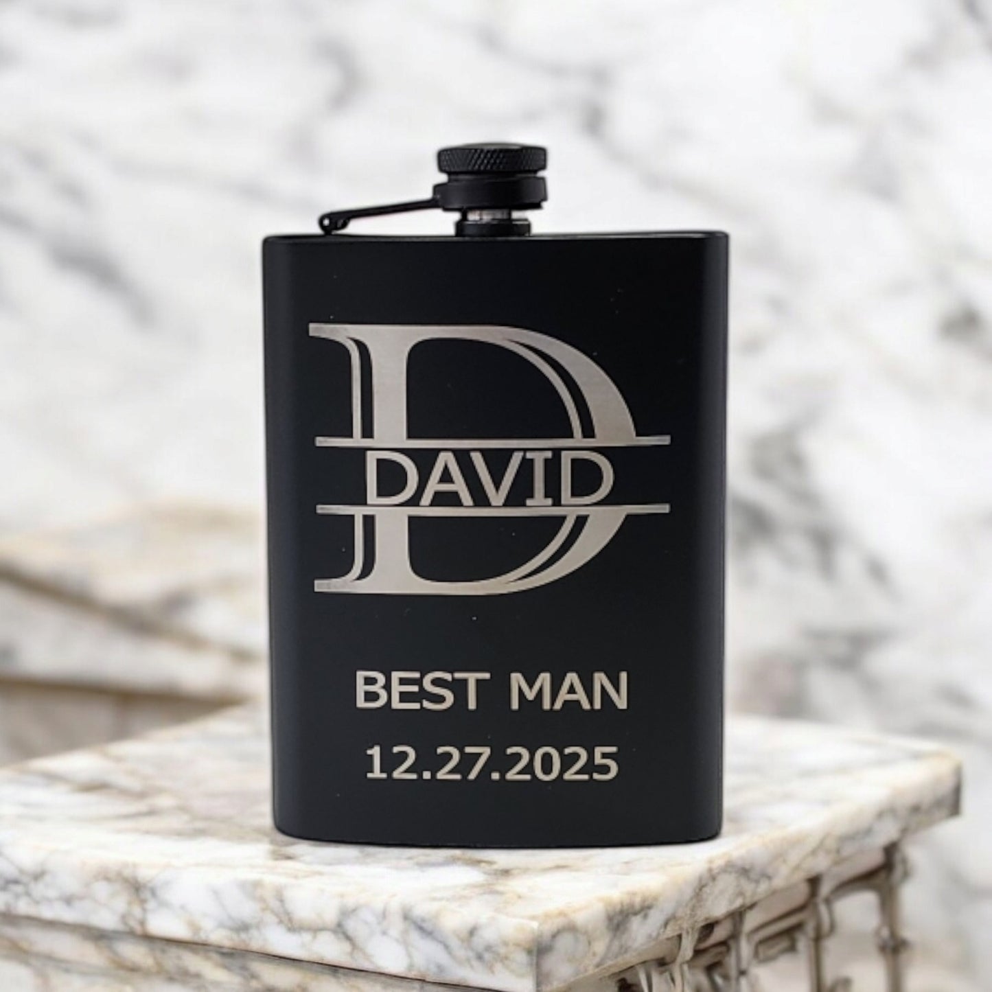 A Mirabilia Boutique Personalized Matte Black Hip Flask rests gracefully on marble, custom engraved with "David," "Best Man," and "12.27.2025." This stylish keepsake is perfect for any memorable occasion.